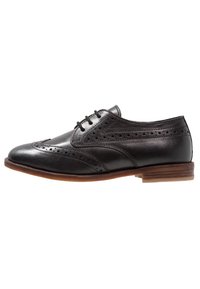 Černé kožené společenské boty s brogue detaily, šněrováním a hnědou koženou podrážkou. Hladká textura a klasický design.