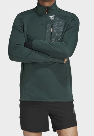 Ciemnozielona sportowa bluza z zamkiem, z fakturowanym materiałem, z wzorem na klatce piersiowej i kieszonką na zamek, w połączeniu z czarnymi szortami.