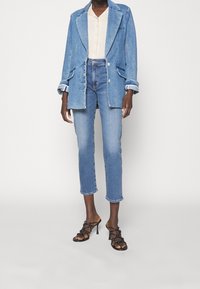 Denimový blazer v světle modré barvě s klopovým límcem a dvěma předními kapsami, doplněný o světle modré cropped džíny a černé sandály na podpatku se strapci.