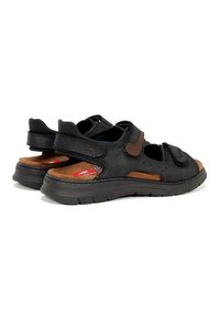 Sandalias de cuero negro con acentos marrones, que cuentan con correas de velcro, secciones recortadas y suelas texturizadas para mayor tracción.
