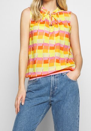 Mouwloze geel, oranje en roze blouse met patroon en strikdetail bij de hals, gedragen met blauwe denim jeans.