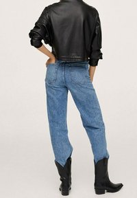 Veste courte en cuir noir, jean bleu clair taille haute et bottines noires. Caractéristiques : coupe décontractée et coutures visibles.