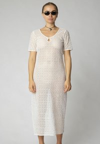 Valge pitsist midi kleit lühikeste varrukatega, teemantmustriga, võtmekaela detailiga ja lahtise lõikega, kanda tumedate prillidega.