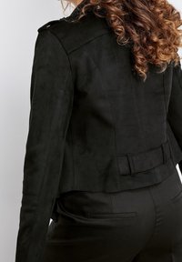Veste en suède noire au design court, dotée d'une taille ceinturée et d'une texture lisse. La vue arrière montre les détails de couture et un col à revers.