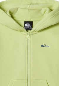 Lichtgroene rits hoodie gemaakt van zachte stof, met een klein marineblauw logo op de borst en kangoeroezakken aan de voorkant.