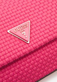 Sac en simili cuir rose tissé avec une plaque métallique triangulaire portant le nom de la marque et un détail point d'interrogation.