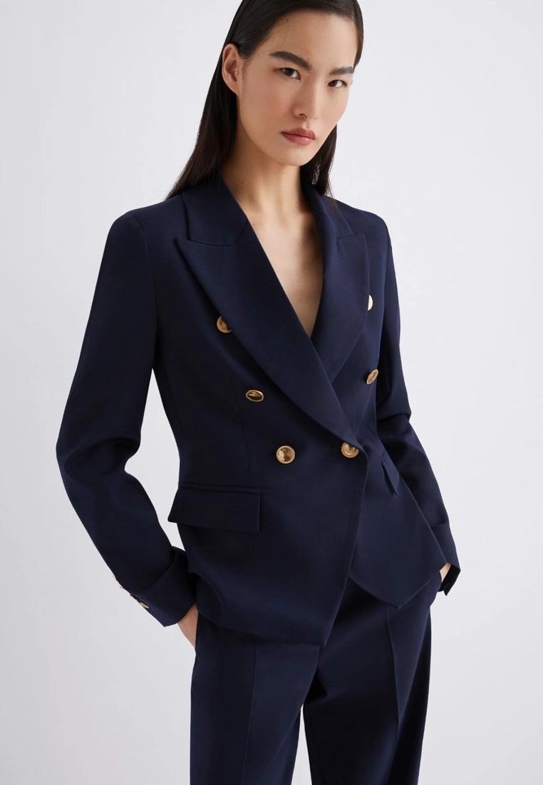 Blazer doppiopetto blu navy realizzato in tessuto liscio, con bottoni dorati, rever a punta e vestibilità su misura, completo di tasche laterali.