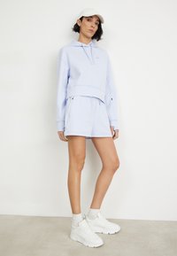 Hanorac scurt de culoare albastru deschis, cu șnur, asortat cu șorturi identice. Adidași albi și o șapcă completează ținuta. Textură netedă în întreaga compoziție.