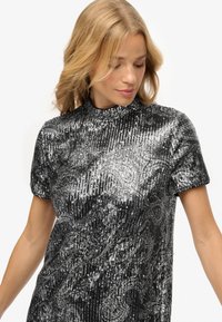Top de lentejuelas negras y plateadas con cuello alto y mangas cortas, que presenta un patrón texturizado en forma de ola en toda su superficie.