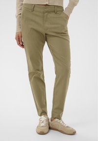 Pantalon kaki avec une coupe effilée, fabriqué dans un tissu léger. Doté de poches avant et d'une texture lisse, accompagné de baskets beige.