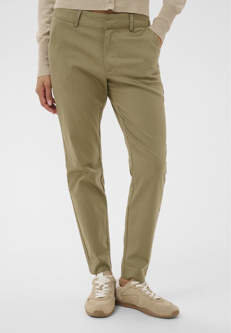 Pantalon kaki avec une coupe effilée, fabriqué dans un tissu léger. Doté de poches avant et d'une texture lisse, accompagné de baskets beige.