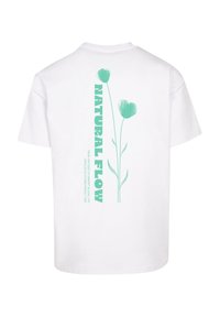 Hvid t-shirt med en grafik på ryggen, der viser to grønne stiliserede blomster og teksten "NATURAL FLOW" i fede, opretstående bogstaver.