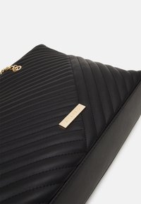 Black quilted faux leather bag featuring a chevron pattern, gold-tone hardware, and an embossed brand logo plate.