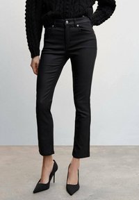 Černé džíny s vysokým pasem a moderním slim fit střihem, se předními kapsami, knoflíkovým zapínáním a hladkým povrchem, doplněné černými špičatými podpatky.