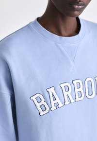 Világoskék pulóver kerek nyakkal, fehér hímzett "BARBOUR" felirattal. Puha anyag finom textúrával és varrási részletekkel.