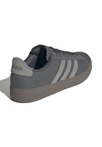 Sneakers Adidas grigi con una toma in tessuto testurizzato. Presentano tre strisce grigie più scure, un colletto imbottito e una suola in gomma. Logo impresso sul tallone.