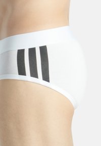 Slip in cotone bianco con un design a tre righe nere sul lato, dotato di un morbido cinturino elastico per il massimo comfort.