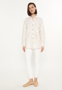 Witte blouse met een subtiele dierenprint, voorzien van borstzakken en lange mouwen. Draag het met witte broeken en lichtbruin schoenen.