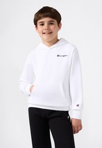 Sudadera blanca con capucha y bolsillo frontal, con un logo bordado; combinada con pantalones de chándal negros que presentan un pequeño logo en la pierna.