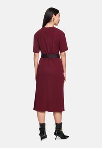 Bordeauxfarbenes Midikleid mit kurzen Ärmeln und einem schwarzen Gürtel in der Taille. Glattes Material; minimalistische Nähte und runder Ausschnitt.
