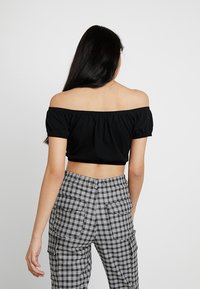 Svart off-the-shoulder cropped topp med puffärmar, kombinerat med högmidjade rutiga cargo-byxor som har flera fickor.