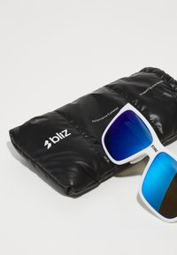 Occhiali da sole bianchi con lenti blu sfumate, poggiati su un morbido astuccio imbottito nero contrassegnato con "bliz Performance Eyewear."