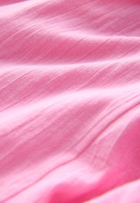 Tissu rose doux avec des plis subtils et une texture fine, montré en gros plan.