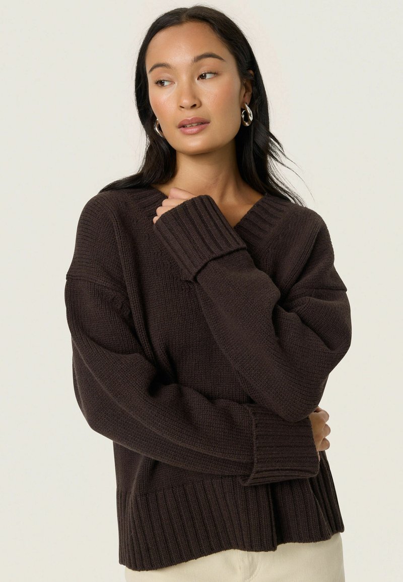 Pull en tricot marron foncé avec un col en V, des poignets côtelés et une coupe décontractée. La texture semble douce avec des motifs en tricot horizontaux.
