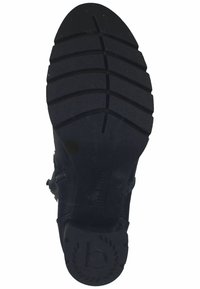 Semelle de bottine noire à épaisse semelle crantée, bout arrondi, et un logo circulaire avec un "b" au talon.