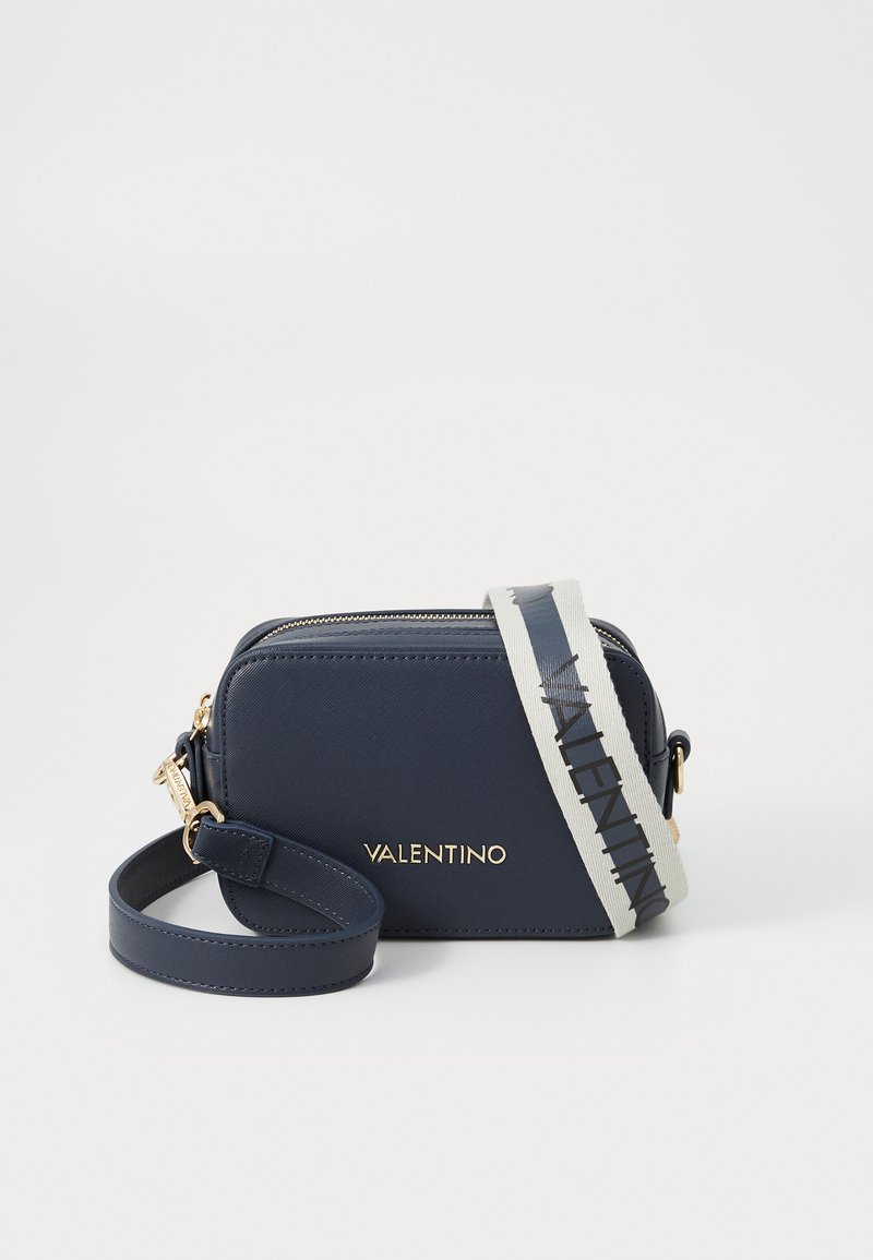 Sac bandoulière en cuir bleu marine avec quincaillerie dorée et une bandoulière contrastante arborant un texte de logo. Forme rectangulaire avec fermeture éclair et bandoulière détachable.
