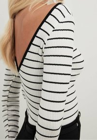 Ribbad långärmad topp i vitt med svarta horisontella ränder, med en djup V-back design och kontrasterande svart trim längs halsringningen.