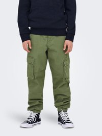 Pantaloni cargo di colore verde oliva, in materiale cotone, con tasche laterali, polsini a gamba affusolata e vestibilità rilassata. Abbinati a scarpe sportive nere alte.