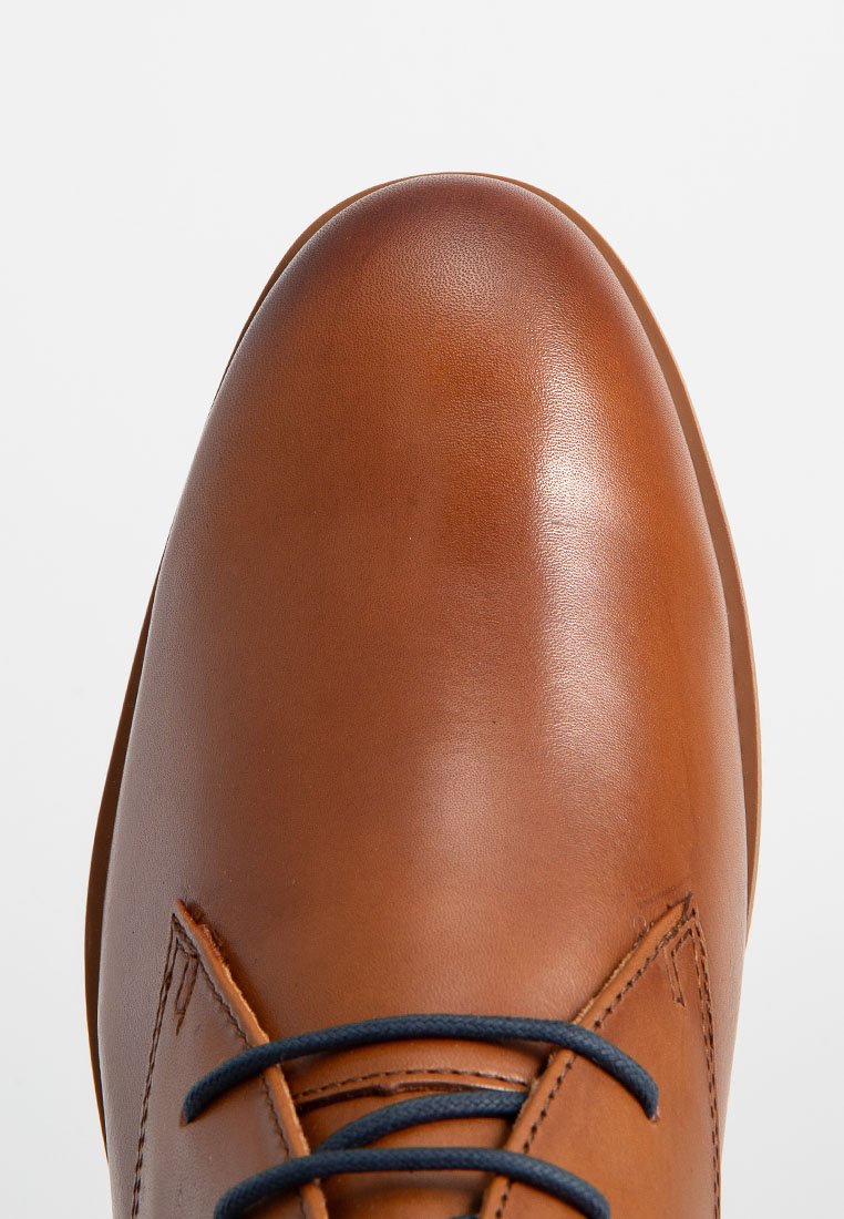 Braunes Leder-Schuh mit abgerundetem Zeh, glatter Textur und dunkelblauen Schnürsenkeln. Verfügt über subtile Nähte und ein elegantes, modernes Design.