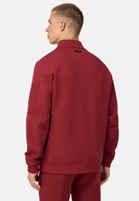 Burgunderfarbener Pullover, weiches Material, hoher Kragen und gerippte Bündchen. Verfügt über eine aufgenähte Tasche am linken Ärmel und ein minimalistisches Design.