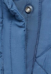 Niebieska tkanina o pikowanej fakturze z widocznym ściegiem; zawiera srebrny zatrzask i lekko marszczone brzegi.