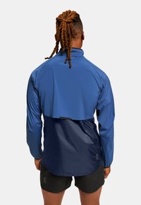 Blue and navy running jacket with a high collar, long sleeves, and a cropped back design; features a lightweight, water-resistant material.
