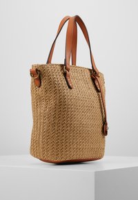 Geweven stro tote tas met tan lederen accenten, gestructureerde vorm, dubbele handgrepen en kleine metalen details, die een natuurlijke textuur creëren.