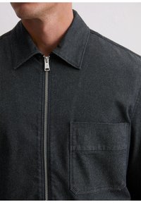 Donkergrijze spijkerjasje met kraag, ritssluiting aan de voorkant en borstzak; voorzien van een gladde textuur en minimalistisch ontwerp.