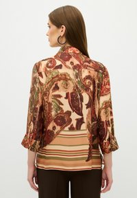 Blouse multicolore avec un motif paisley en rouge et vert, au design fluide, avec des manches trois-quarts et des accents de ourlet rayés.