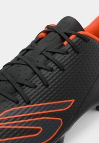 Svart fotballsko med teksturert overdel, oransje detaljer og svarte lisser. Har et strømlinjeformet design med en fremtredende logo.