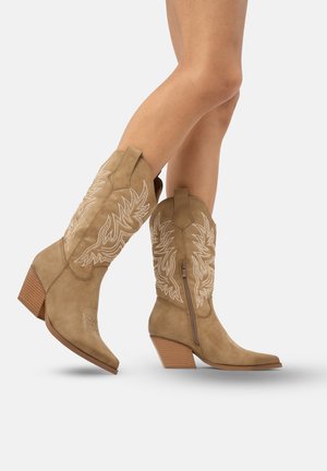 Bottes western en daim tan avec des pointes pointues, des motifs brodés blancs complexes et un talon carré empilé ; fermeture éclair sur le côté pour un enfilage facile.