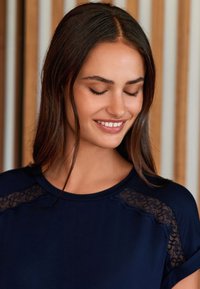 Haut bleu marine avec des accents en dentelle sur les épaules, un col rond et une texture douce. Le modèle est à coupe décontractée avec des manches courtes.