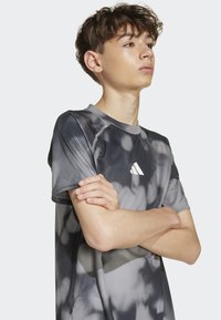 Šedé športové tričko s batikovaným vzorom, krátkym rukávom a okrúhlym výstrihom. Obsahuje biele logo na hrudi a kontrastné stehy.