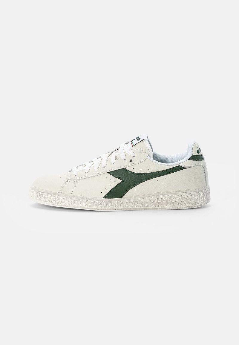 White leather sneaker featuring a green diagonal stripe, a textured rubber sole, and white laces, with subtle perforations and branding.