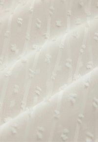 Tissu blanc avec un motif texturé de petits points en relief et de rayures verticales dans un matériau doux et léger.