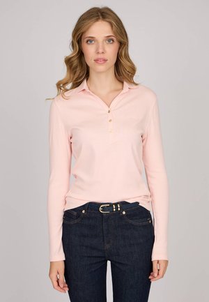 Polo à manches longues en coton rose doux avec un col, doté de trois boutons dorés. Associé à un jean bleu foncé et une ceinture noire.