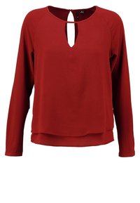 Blouse à manches longues rouge rouille avec ourlet superposé et encolure fendue à l'avant, en tissu texturé.