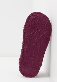 Lila toffelbotten med strukturerad, vågig mönstring. Mjukt material med stickade kanter och en lätt kurva. Platt sko utan klack.