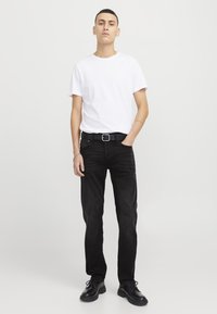 Jeans neri e una maglietta bianca aderente, abbinati a una cintura nera e scarpe stringate nere. Design semplice, texture liscia e colori neutri.
