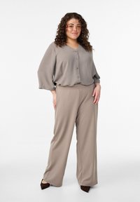 Bež bluza z zaobljenim izrezom in gumbi, kombinirana z visokim pasom hlač v enakem gladkem, tekočem materialu.